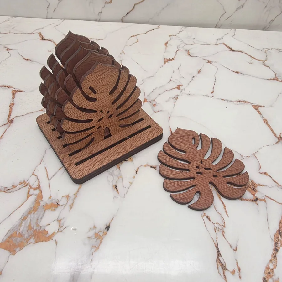 Slotted wooden stand holding monstera leaf coasters upright, with one coaster lying beside it
